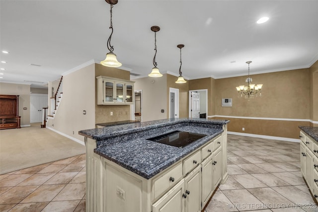 kitchen with pendant lighting, cream cabinets, black electric stovetop, dark stone countertops, and an island with sink