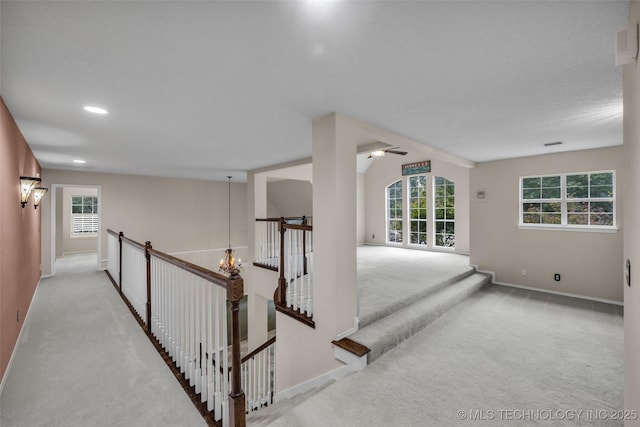 corridor with a chandelier, light colored carpet, plenty of natural light, and lofted ceiling