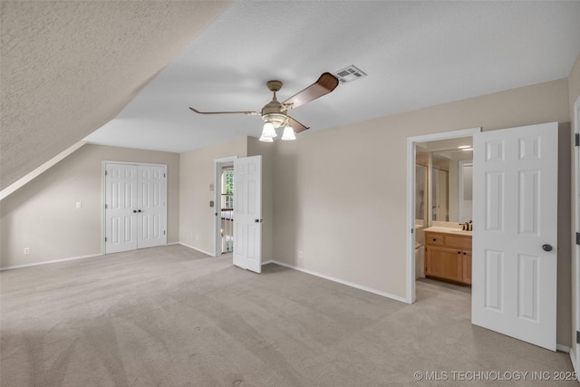 unfurnished bedroom featuring ensuite bath, a textured ceiling, ceiling fan, a closet, and lofted ceiling