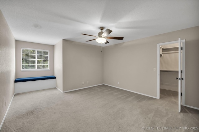 unfurnished bedroom featuring light carpet, a spacious closet, a ceiling fan, and baseboards