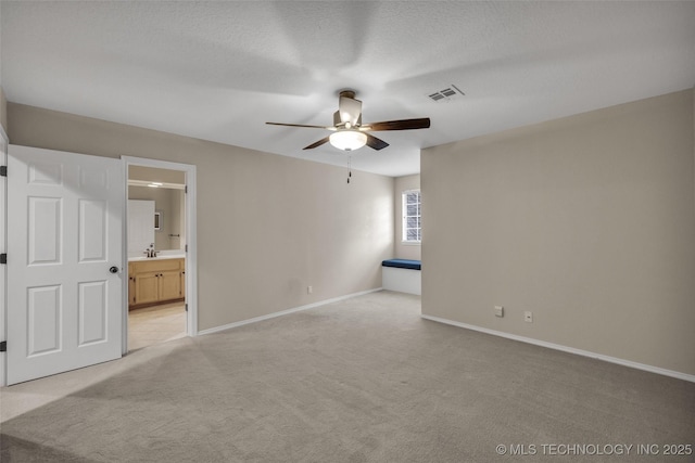 unfurnished bedroom featuring visible vents, light carpet, a sink, a textured ceiling, and baseboards