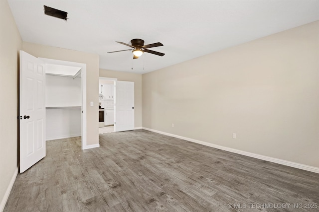 unfurnished bedroom with ceiling fan, a closet, a spacious closet, and wood-type flooring