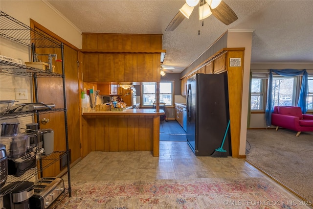 kitchen featuring kitchen peninsula, black fridge, a textured ceiling, light colored carpet, and a healthy amount of sunlight