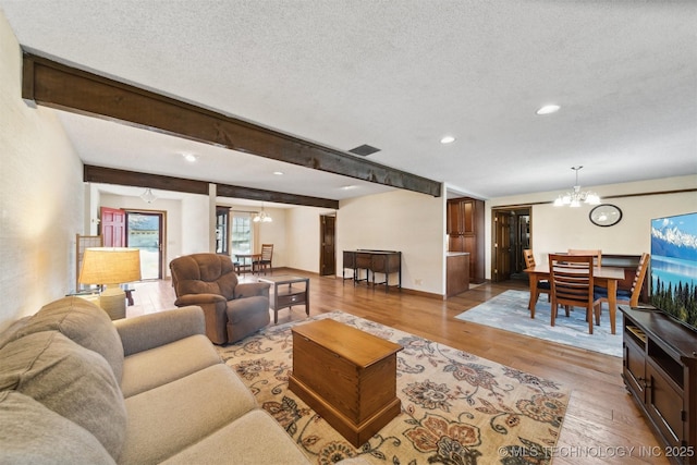 living room with beam ceiling, an inviting chandelier, a textured ceiling, and light wood-type flooring