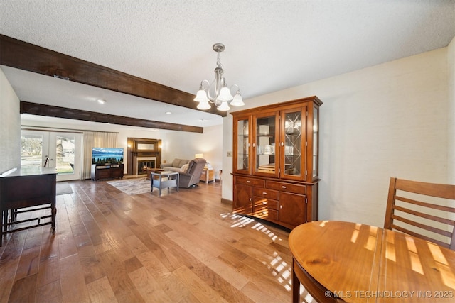 dining room featuring french doors, hardwood / wood-style flooring, a textured ceiling, beam ceiling, and a chandelier