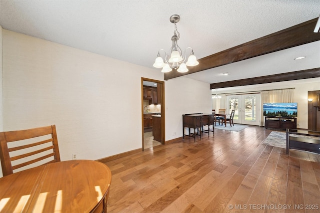 dining area featuring french doors, sink, wood-type flooring, an inviting chandelier, and beamed ceiling