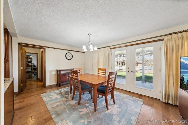 dining space featuring french doors, a textured ceiling, a notable chandelier, and hardwood / wood-style floors