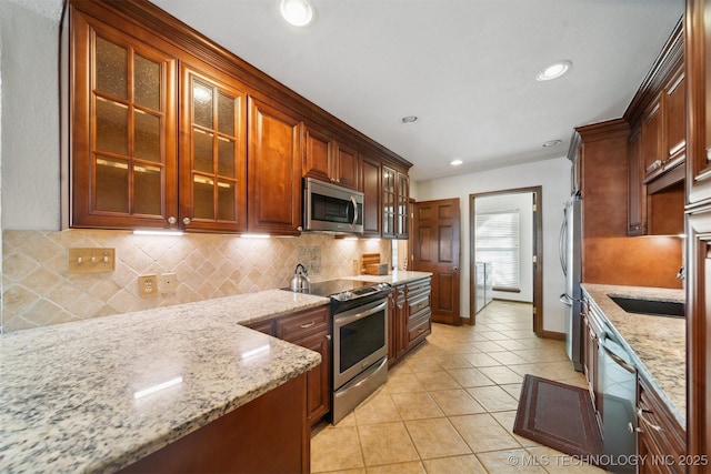 kitchen with light stone countertops, sink, stainless steel appliances, decorative backsplash, and light tile patterned floors