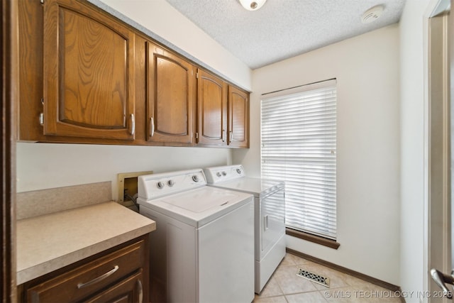 clothes washing area featuring washing machine and clothes dryer, light tile patterned flooring, cabinets, and a textured ceiling