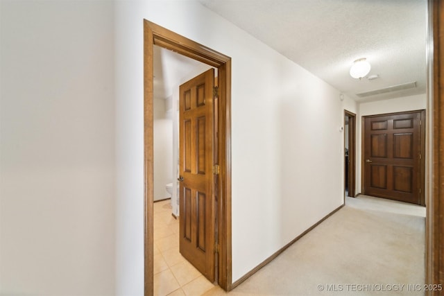 corridor featuring a textured ceiling and light carpet