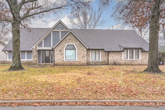 english style home featuring stone siding, a shingled roof, and a front lawn