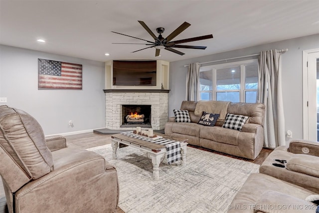 living room featuring ceiling fan, light wood-type flooring, and a fireplace