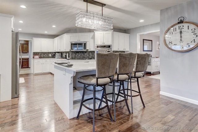 kitchen featuring backsplash, white cabinets, hanging light fixtures, appliances with stainless steel finishes, and wood-type flooring