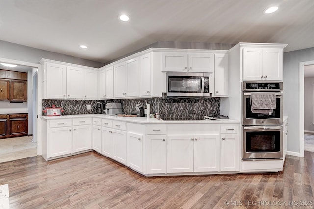 kitchen with light wood-type flooring, white cabinetry, backsplash, and appliances with stainless steel finishes