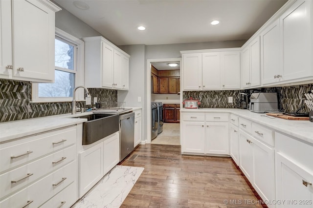 kitchen featuring sink, tasteful backsplash, washing machine and dryer, stainless steel dishwasher, and white cabinets