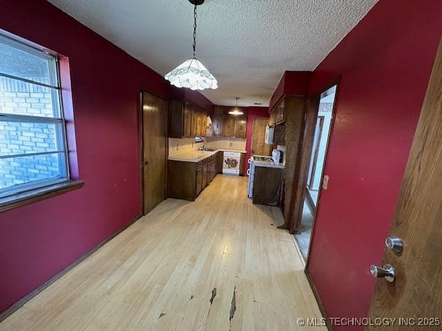 kitchen with a textured ceiling, hanging light fixtures, and light hardwood / wood-style flooring