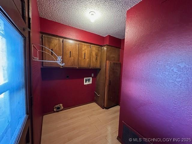 washroom with cabinets, hookup for a washing machine, a textured ceiling, electric dryer hookup, and light hardwood / wood-style floors