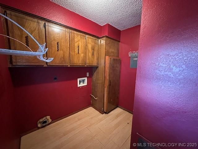 clothes washing area with cabinets, washer hookup, a textured ceiling, electric dryer hookup, and light hardwood / wood-style flooring