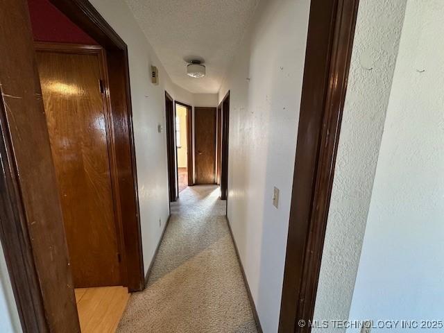 hallway featuring a textured ceiling and light carpet