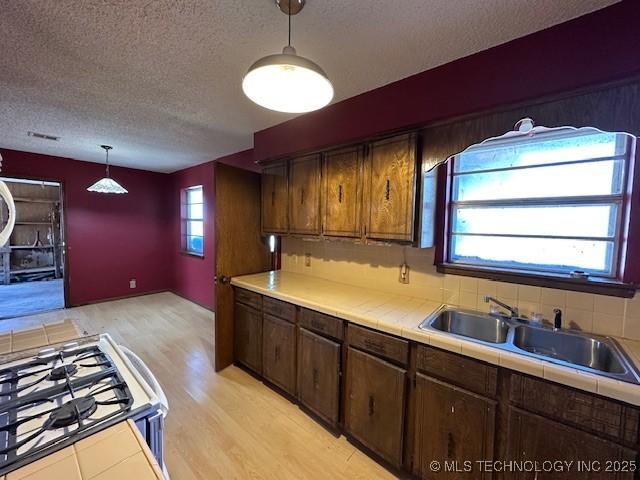 kitchen featuring sink, hanging light fixtures, tile countertops, light hardwood / wood-style floors, and a textured ceiling