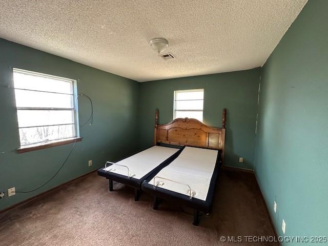 unfurnished bedroom with a textured ceiling and dark colored carpet