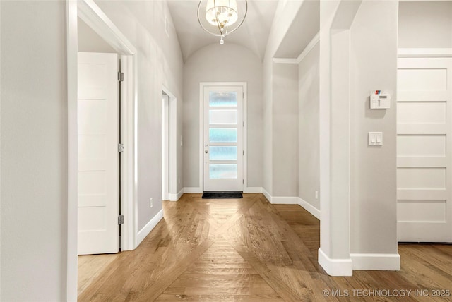 doorway featuring vaulted ceiling, an inviting chandelier, and light wood-type flooring