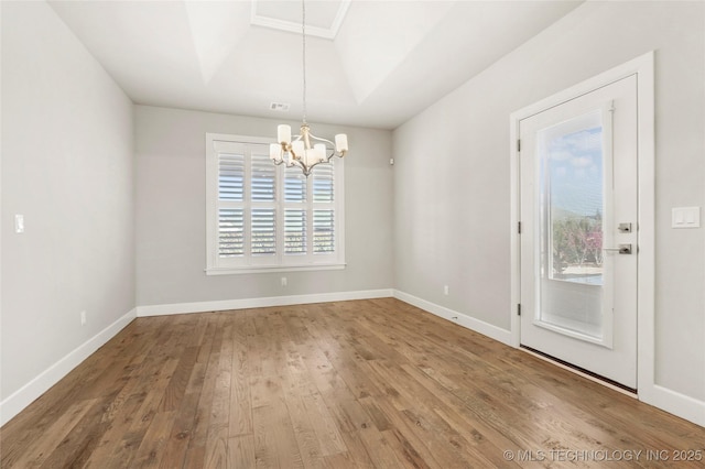 unfurnished dining area with wood-type flooring, a raised ceiling, and a notable chandelier