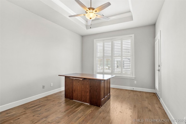 unfurnished office featuring a raised ceiling, ceiling fan, and hardwood / wood-style flooring