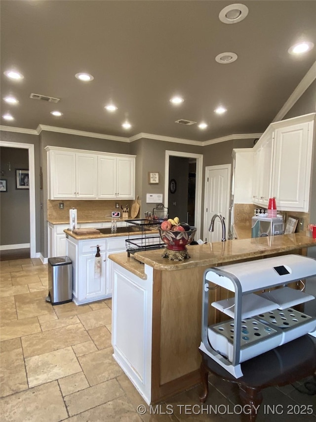 kitchen featuring white cabinetry, sink, tasteful backsplash, crown molding, and an island with sink