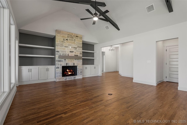 unfurnished living room featuring ceiling fan with notable chandelier, dark wood-type flooring, beam ceiling, built in features, and a stone fireplace