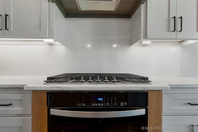 kitchen with backsplash, black oven, white cabinetry, and light stone countertops