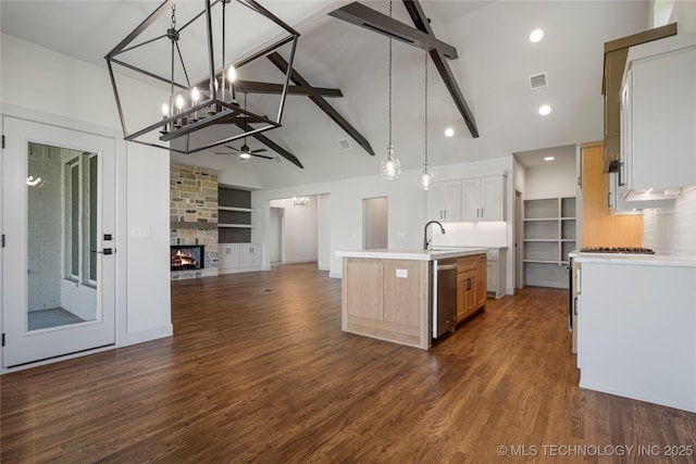 kitchen with white cabinetry, hanging light fixtures, built in features, stainless steel dishwasher, and a kitchen island with sink