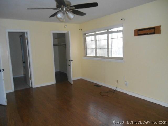 unfurnished bedroom featuring ceiling fan, dark hardwood / wood-style flooring, a walk in closet, and a closet