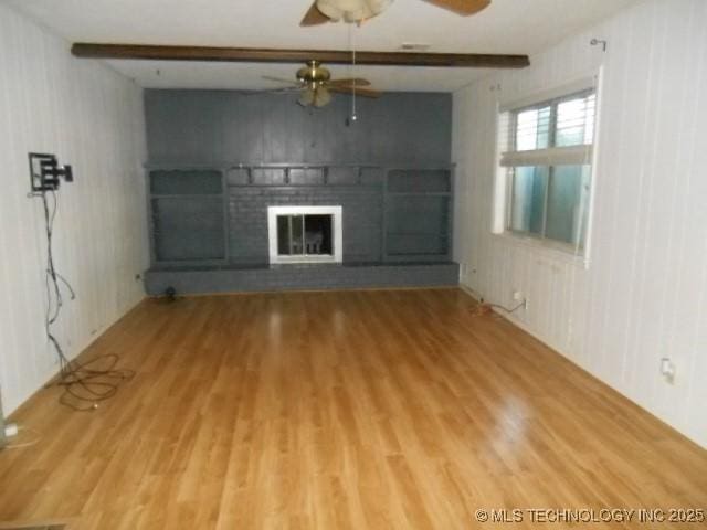 unfurnished living room featuring wood walls, ceiling fan, a fireplace, beam ceiling, and wood-type flooring