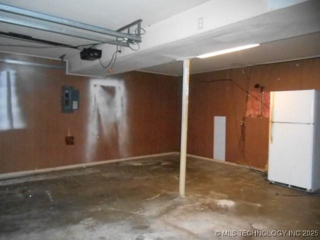 garage featuring electric panel, white fridge, a garage door opener, and wooden walls