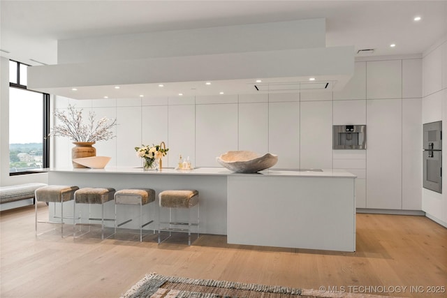 kitchen featuring a kitchen breakfast bar, a spacious island, white cabinetry, and light wood-type flooring