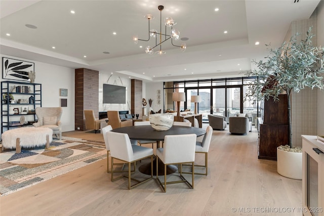 dining room with floor to ceiling windows, a raised ceiling, light wood-type flooring, and a chandelier