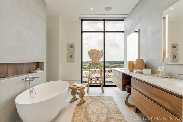 bathroom featuring expansive windows, vanity, tile walls, tile patterned flooring, and a bathing tub