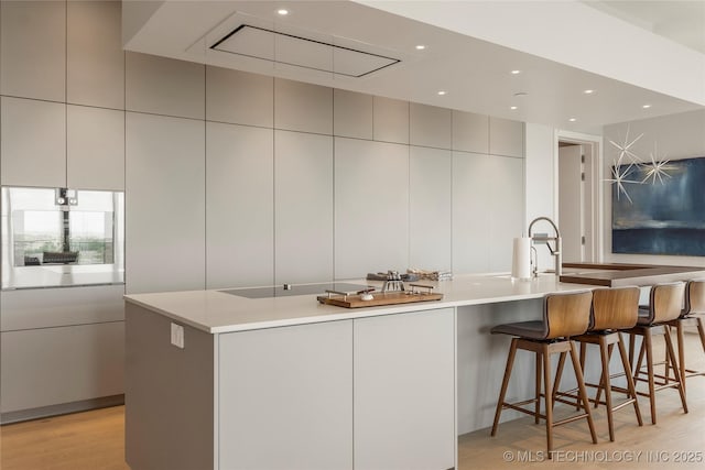 kitchen featuring a kitchen breakfast bar, a large island with sink, tile walls, and light wood-type flooring