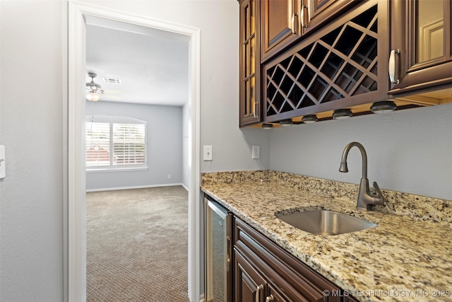 kitchen featuring carpet flooring, light stone counters, ceiling fan, beverage cooler, and sink