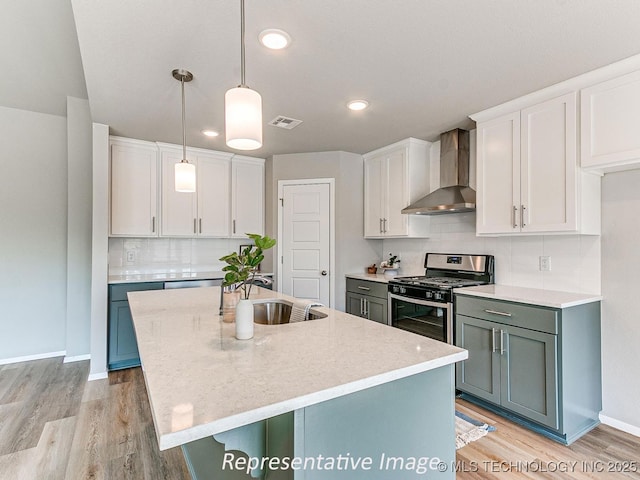 kitchen featuring white cabinets, pendant lighting, wall chimney exhaust hood, and stainless steel gas range