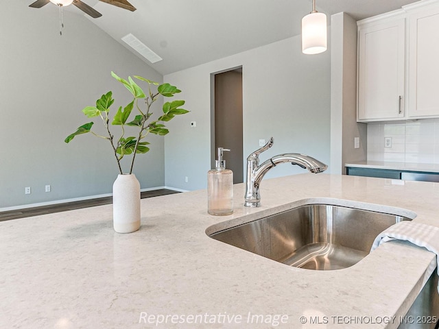 kitchen featuring pendant lighting, lofted ceiling, white cabinets, sink, and tasteful backsplash