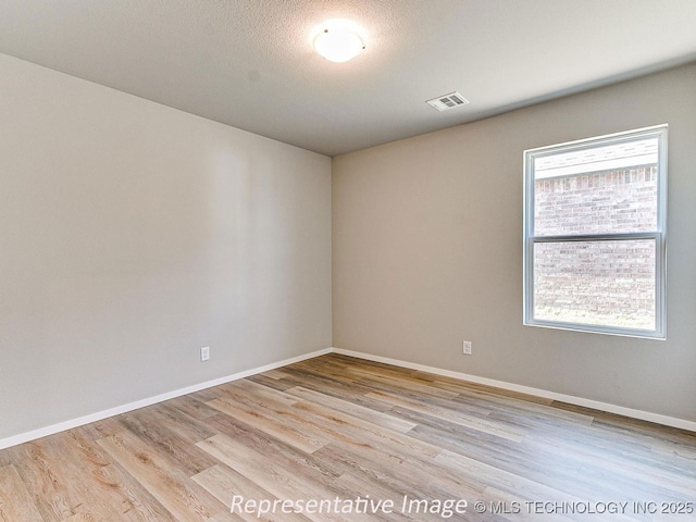 spare room featuring plenty of natural light, light wood-type flooring, and a textured ceiling