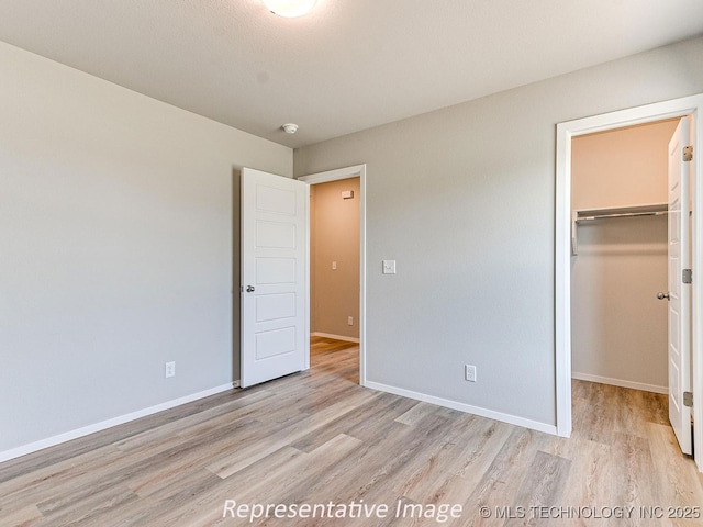 unfurnished bedroom with light wood-type flooring, a spacious closet, and a closet