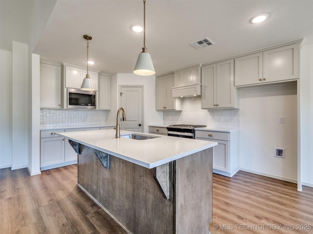 kitchen featuring visible vents, a kitchen island with sink, a sink, stainless steel appliances, and light wood-type flooring