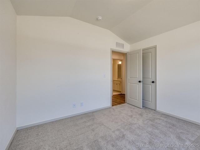 unfurnished bedroom featuring visible vents, baseboards, carpet, and vaulted ceiling