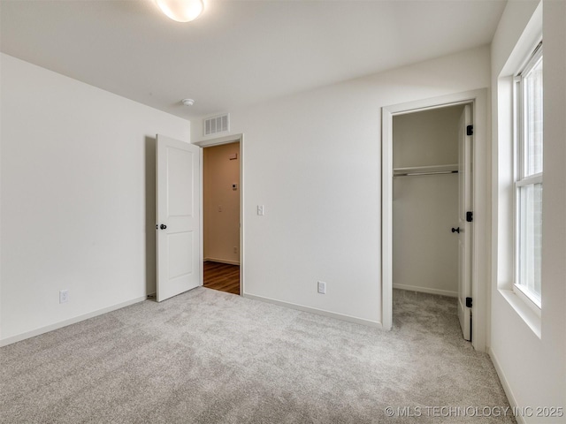 unfurnished bedroom with a spacious closet, visible vents, baseboards, carpet, and a closet