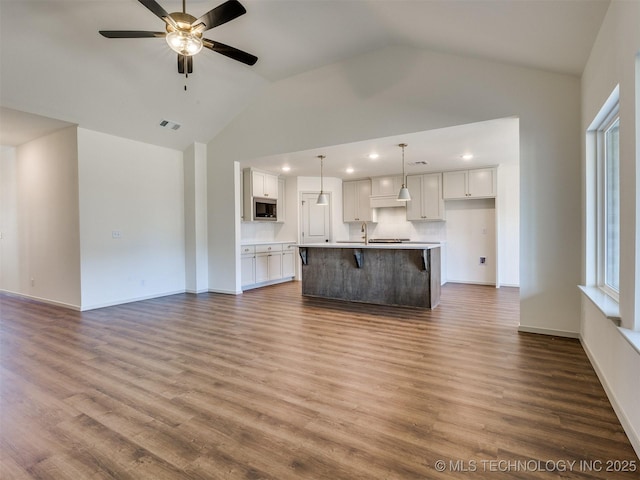 unfurnished living room with visible vents, a ceiling fan, a sink, dark wood finished floors, and baseboards