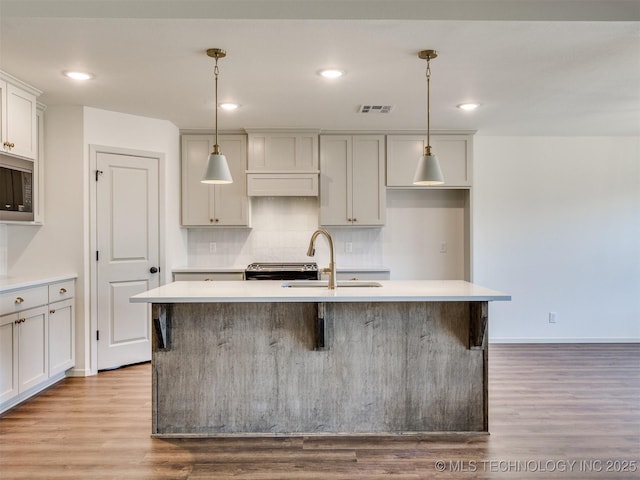 kitchen featuring tasteful backsplash, visible vents, an island with sink, wood finished floors, and a sink