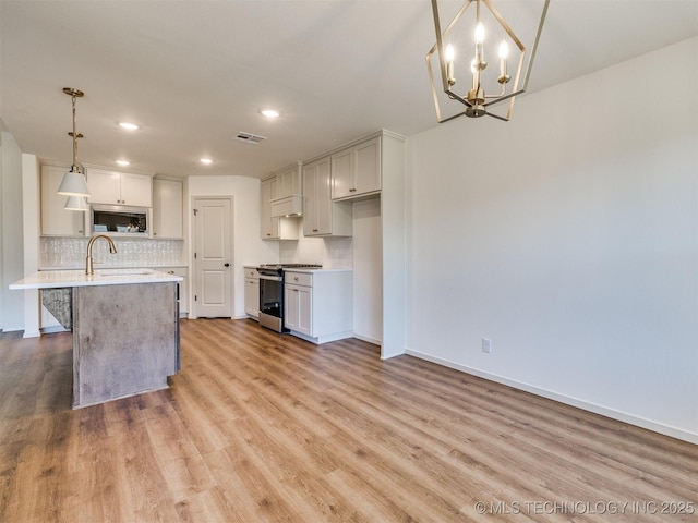 kitchen with light wood finished floors, a sink, decorative backsplash, light countertops, and appliances with stainless steel finishes